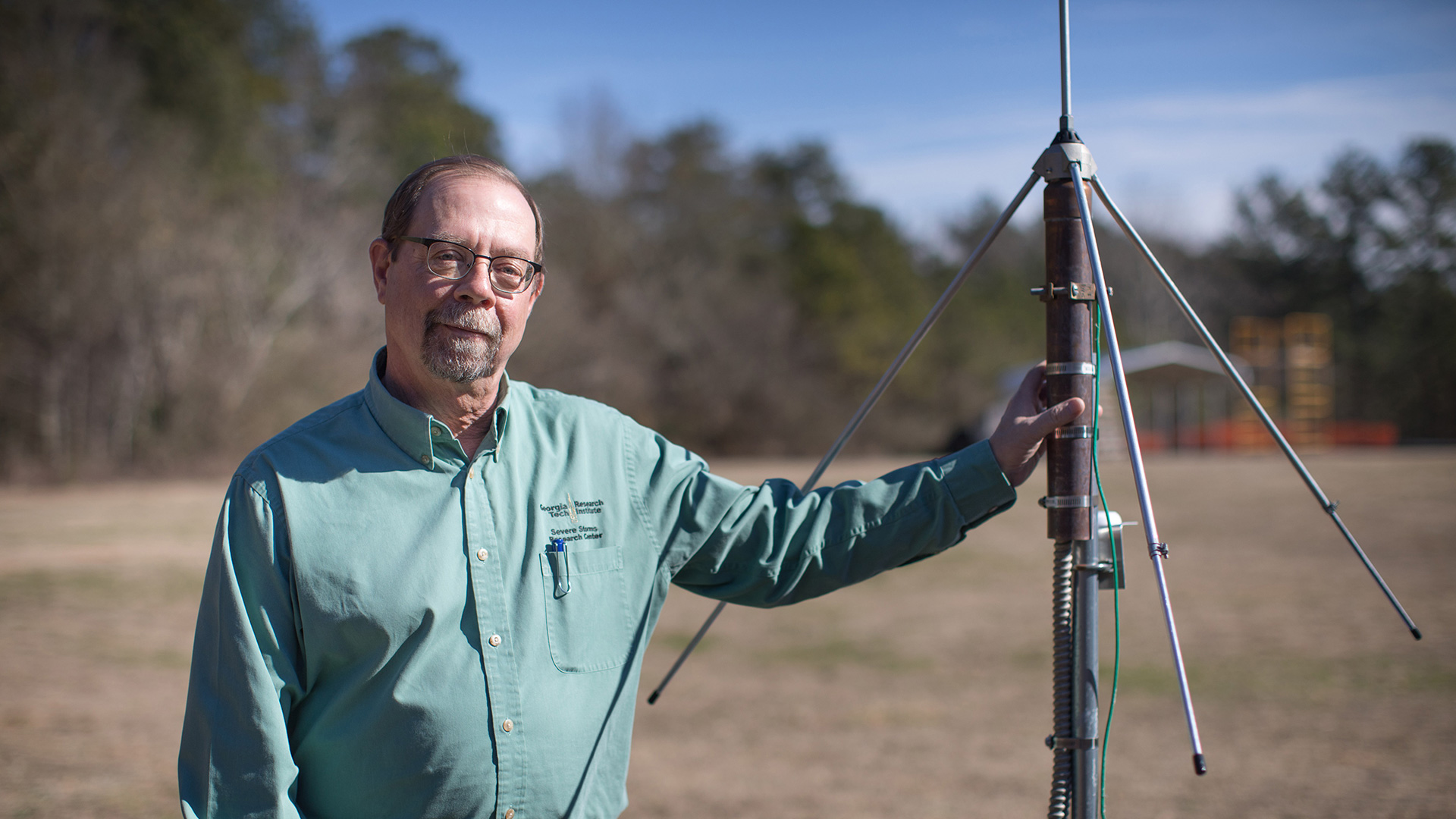photo: man standing outside in a field, on a crisp Fall day, with hand on weather instrument.