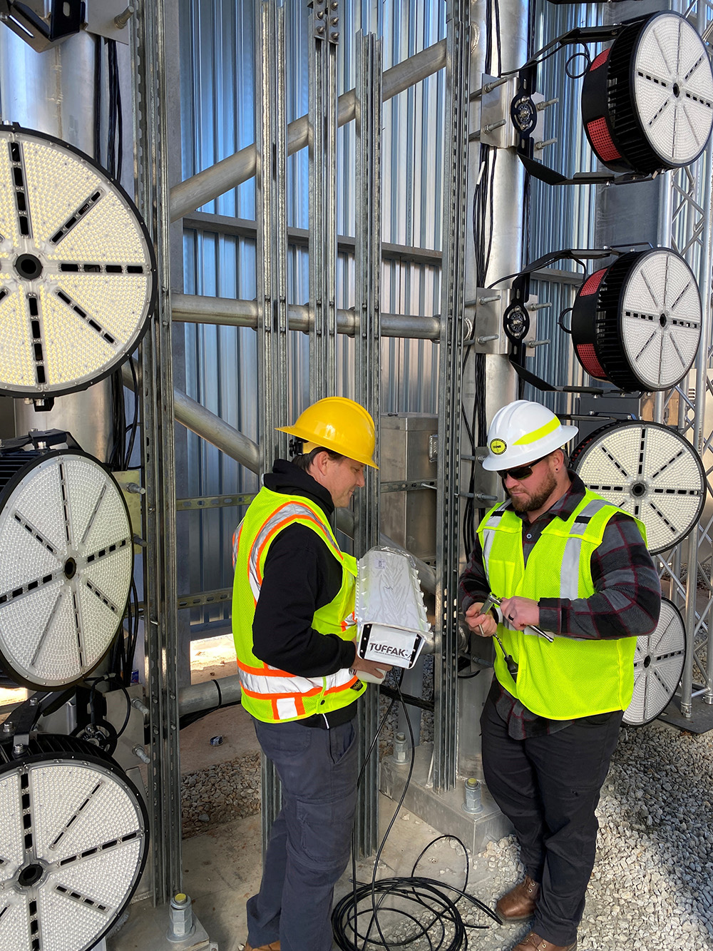 Two workers wearing hard hats and reflective vest talking with each other inside the sheet metal train portal.