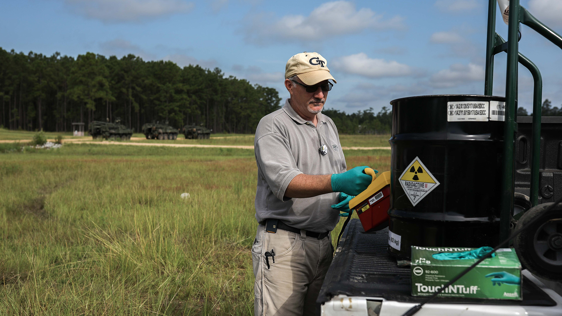 Middle age white male researcher Greg Louden in the field examining a barrel of radioactive material.