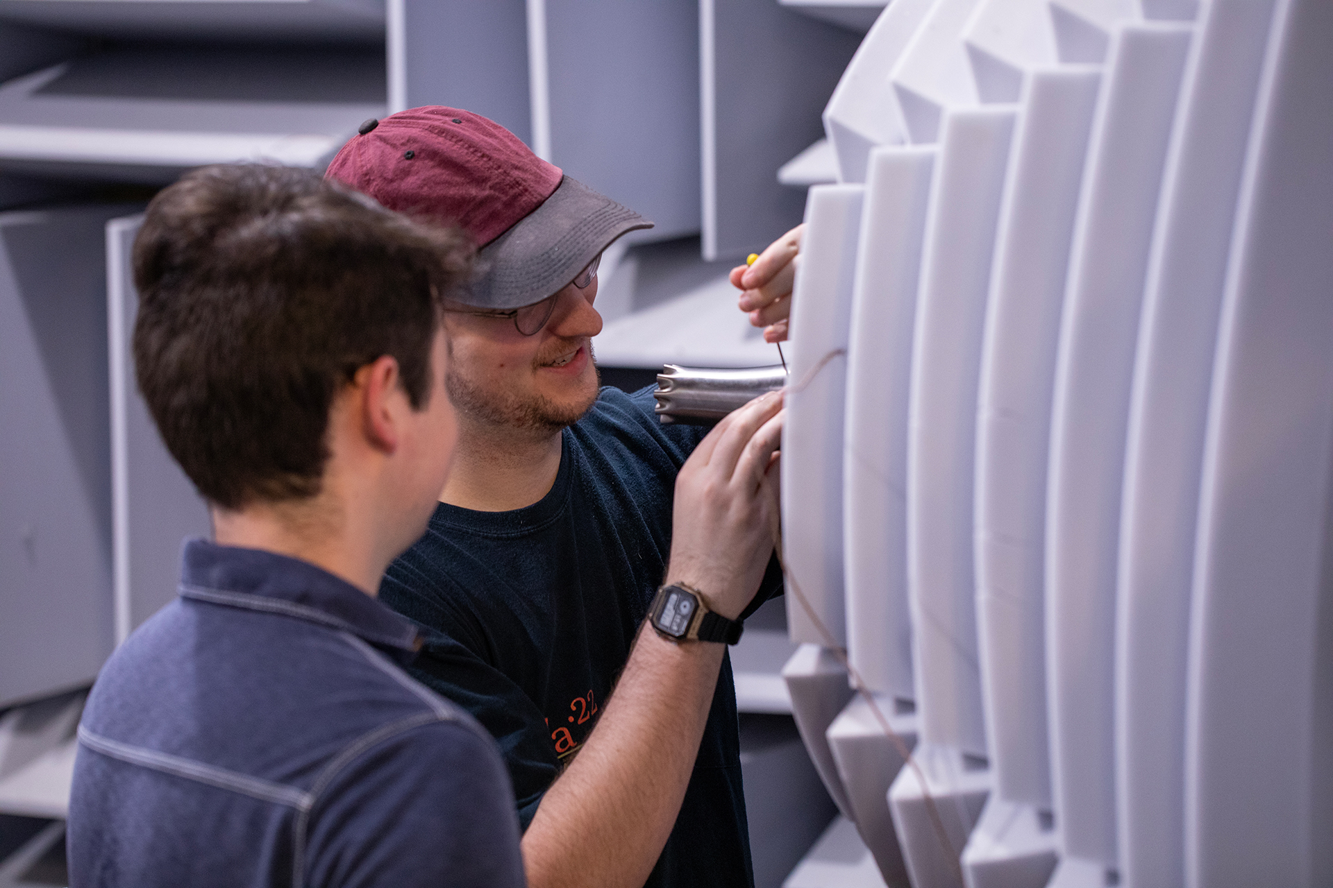 Close up view of two researchers inside a large acoustic chamber examine a nozzle testing device.