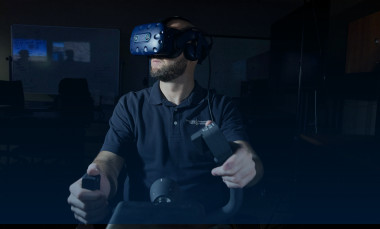 Front view of male researcher wearing VR goggles with hands on flight controls, in a darkened room
